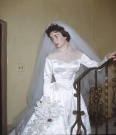 an old photo of a woman in a wedding dress standing on the stairs with her veil over her head