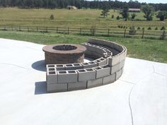 a brick fire pit sitting on top of a cement slab next to a lush green field