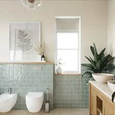 two white toilets sitting next to each other in a bathroom with green tiles on the walls