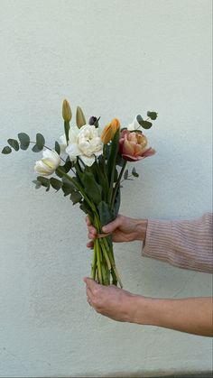 a person holding a bouquet of flowers in their hands with white and yellow flowers on the stems