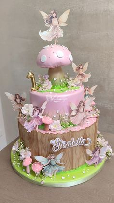 a three tiered cake decorated with pink and green flowers, tinkerbells and fairy figures