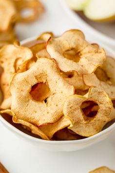 a white bowl filled with apple chips on top of a table next to sliced apples