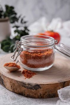 a glass jar filled with spices sitting on top of a wooden board next to a spoon