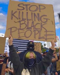 a protester holds up a sign that reads stop killing black people, while wearing a mask