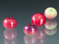 three pomegranates and one apple on a reflective surface