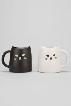 two black and white cats mugs sitting side by side on a gray background, one has a cat's face painted on it