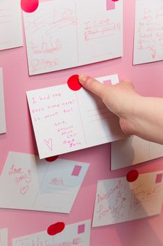 a hand is pointing at some post it notes on a pink wall with red circles