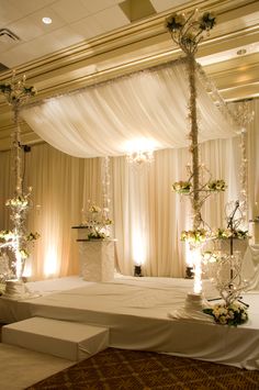 a bed with white drapes and flowers on the headboard is set up for a wedding ceremony