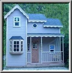 a small blue house sitting in the middle of a field with trees and bushes behind it