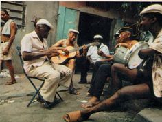 a group of men sitting around each other while playing guitar and singing on the street