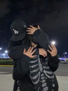 two people hugging each other in front of a parking lot at night with lights behind them