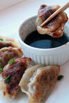 some dumplings with dipping sauce in a white bowl on a plate next to chopsticks