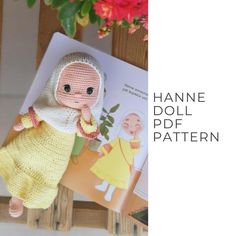 the doll is wearing a knitted outfit and holding a book in her hands with flowers behind it