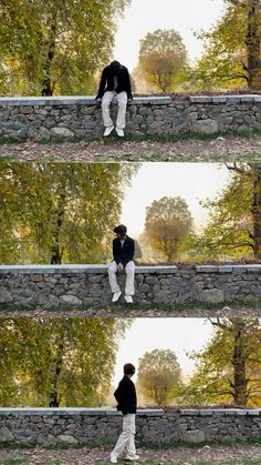 a man sitting on top of a stone wall next to a forest filled with trees