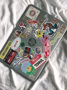 a laptop covered in stickers on top of a white sheet