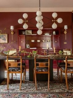 a dining room with red walls and wooden chairs around a black table surrounded by hanging lights