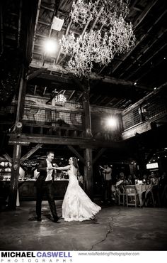 a bride and groom dance together in an old barn at their wedding reception, with chandelier hanging from the ceiling