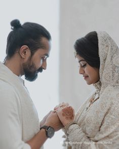 a man and woman standing next to each other looking at something on their hands while wearing white clothing