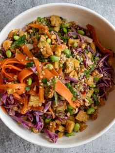 a white bowl filled with carrots, lettuce and other vegetables on top of a table