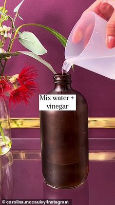 a person pours water into a bottle with flowers in the vase next to it