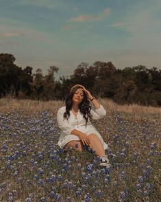 a woman sitting in the middle of a field full of blue wildflowers with her eyes closed