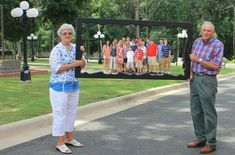 two people standing in front of a memorial with pictures on the wall and trees behind them