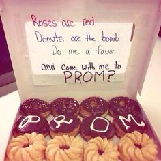 a box filled with lots of donuts sitting on top of a white table next to a sign