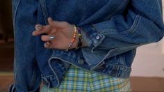 a person wearing a jean jacket and plaid shorts with their hand on her hip pocket