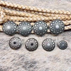 five antique style buttons and rope on a cowhide background, including one with a flower design