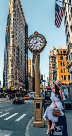 a woman standing next to a tall clock on the side of a road in new york city