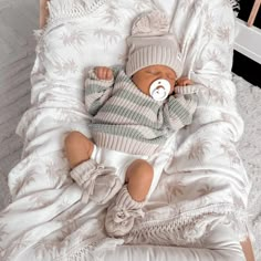 a baby laying in a crib wearing a knitted hat and sweater with a pacifier