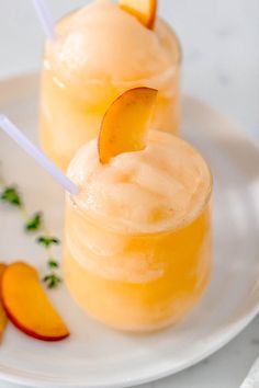 two glasses filled with ice cream and peach slices on a white plate next to sliced oranges