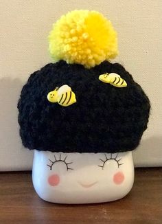 a black hat with yellow pom poms is on top of a white cup