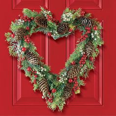 a heart shaped wreath with pine cones and berries hanging on a red door, decorated for christmas