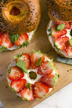 three bagels with strawberries on them and sprinkled with poppy seeds are sitting on a cutting board