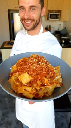 a man holding a plate with pasta and sauce on it