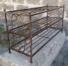 a metal bed frame sitting on top of a cement slab next to a stone wall