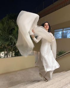 a woman in a white dress is walking down the stairs with her scarf around her neck