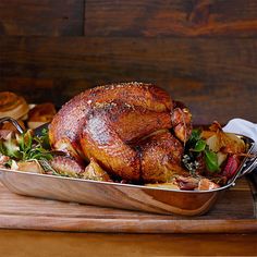 a roasted turkey in a roasting pan on a cutting board with bread and vegetables