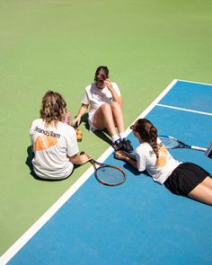 three women sitting on the tennis court with their racquets resting against each other