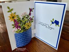 a blue vase filled with flowers sitting on top of a wooden table next to an open card