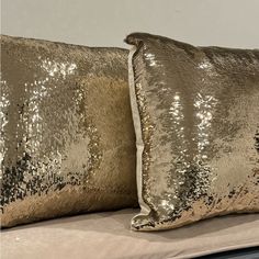 two gold sequin pillows sitting on top of a bed