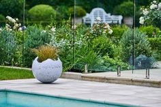 a large white planter sitting on top of a pool next to a lush green field