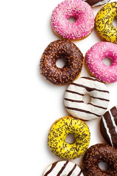 there are many different donuts on the white table and one is pink, yellow, and brown