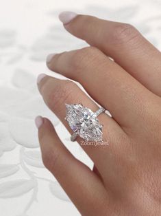 a woman's hand with a diamond ring on top of her finger and an oval shaped diamond in the middle