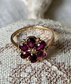 An exquisite Edwardian ring in the shape with 6 precious purple garnet forming a dainty flower with a tiny seed pearl as its heart. We love the high decorated basket that enhances the clarity of the gems. - Size: US 7 3/4; UK P; France 56.5; Numero 16,5 - Weight: 2.3 gr - Dimensions: face is about 1.1 cm diameter; Raises 0.4 cm on top of the finger - Fineness: stamped 14K (yellow gold) - Era: Early 20th century; Art Nouveau style - Condition: Good antique condition; some abrasion to the stones visible with a magnifier; one claw on the side is not attached (which does not compromise the ring's solidity in any way). - Gems: Rhodolite garnets (purple type as opposed to red or wine colour garnets) A most feminine ring with its purplish pink hue that is sure to delight and enhance your finger. Garnet Flower Ring, Unique Antique Rings, Vintage Gem Rings, Vintage Flower Ring, Vintage Jewelry Gold, Art Nouveau Rings, Vintage Ring Stack, Victorian Jewellery Designs, Gem Stone Engagement Rings