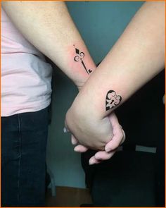 two people are holding hands with tattoos on their arms and one has a key in the middle