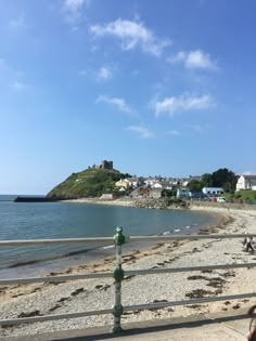 people are walking on the beach by the water's edge with houses in the background