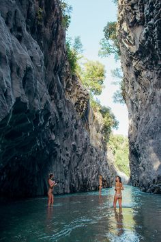 two people are standing in the water near some cliffs