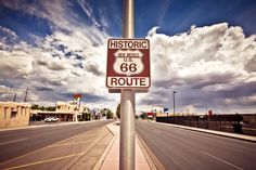 a route 66 sign on the side of an empty road with clouds in the background